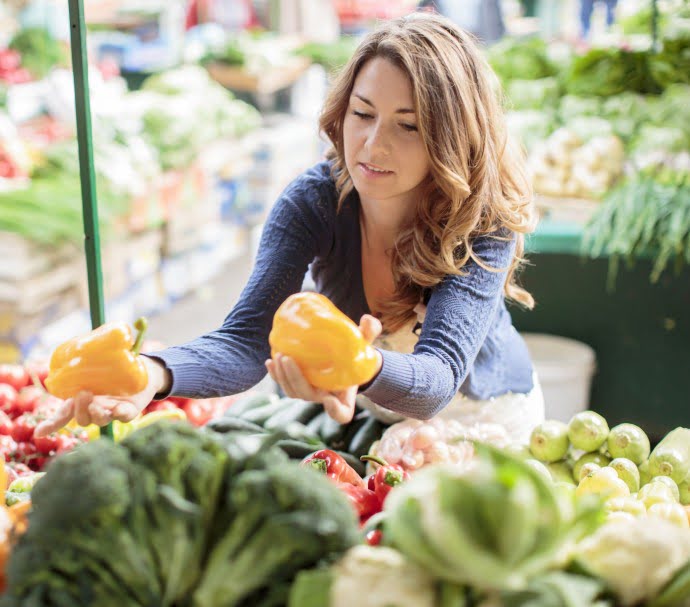 Jeune femme hésitant entre deux poivrons jaune au supermarché